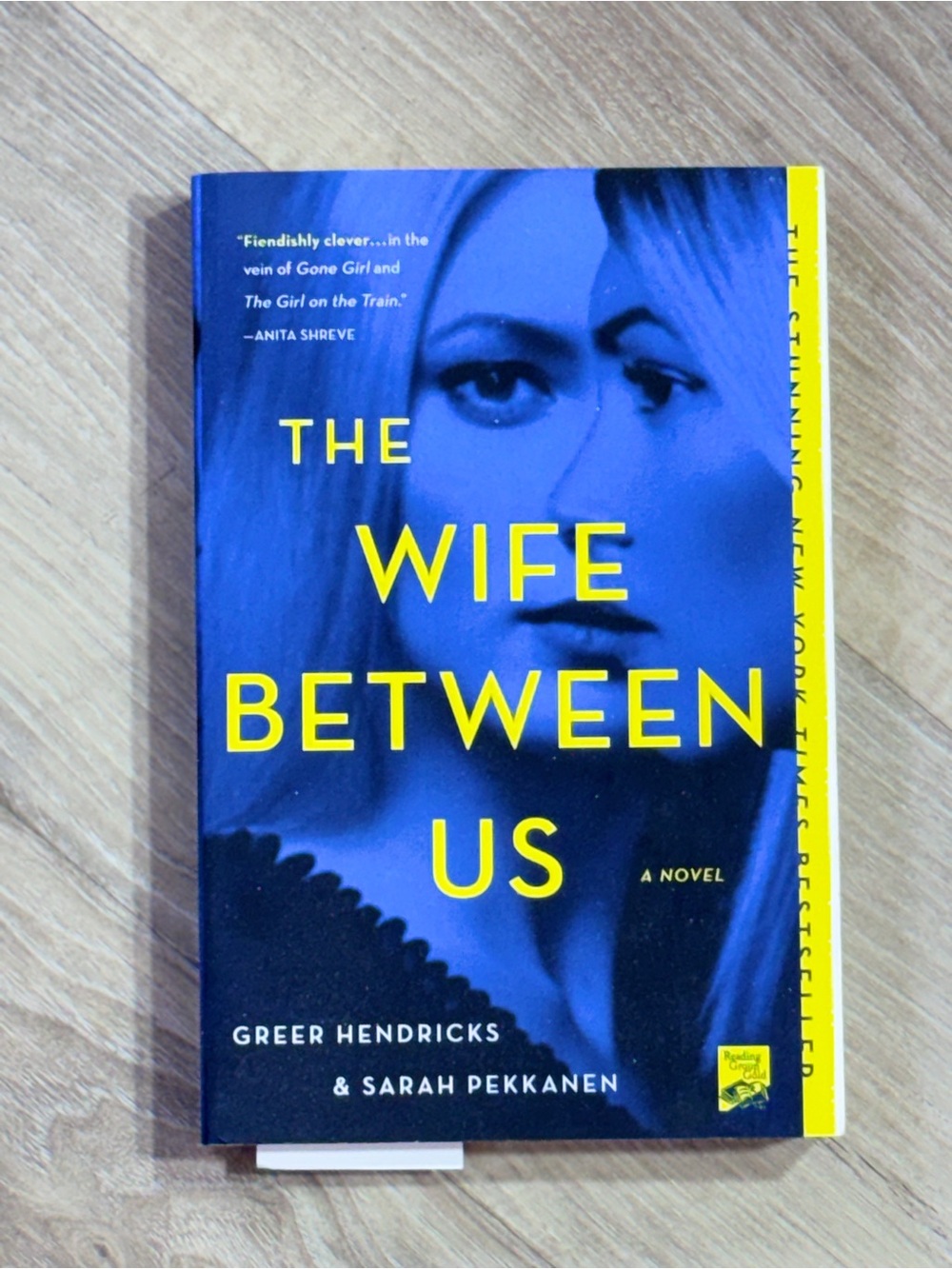 The Wife Between Us — Blue & Yellow Paperback Novel